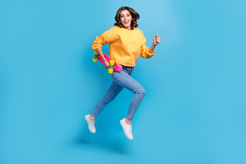 Fototapeta na wymiar Full length photo of sweet cute girl dressed yellow pullover holding skateboard jumping high isolated blue color background