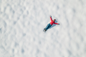 Naklejka na ściany i meble Happy woman lying on the snow at winter, christmas day. Drone, top, aerial view.