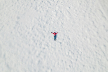 Happy woman lying on the snow at winter, christmas day. Drone, top, aerial view.