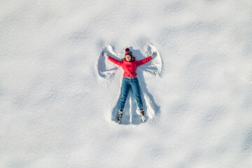 Woman lying on a snow and doing angel print on a snow covered land. Aerial, top view. Drone photo....