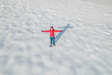 Happy woman, girl in a red winter jacket with spreading her arms standing on snow covered land . Aerial, top view, drone.  Freedom, hope, peace concept