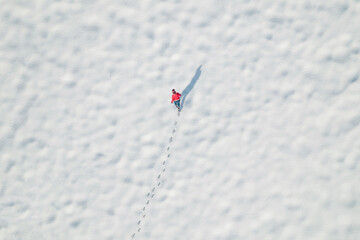 Woman in a red christmas jacket walking on the snow and doing footprints in a park. Winter. Drone, top, aerial view.