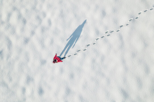 Woman in a red christmas jacket walking on the snow and doing footprints in a park. Winter. Drone, top, aerial view.