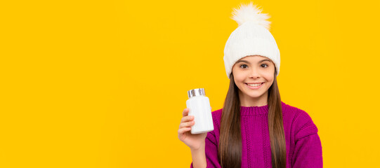 smiling child in winter hat with pill jar. food supplement. teen girl with natural pill products. Horizontal poster of isolated child face, banner header, copy space.