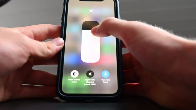 A phone user change the luminosity parameter in the settings, adjusting the brightness to his confort