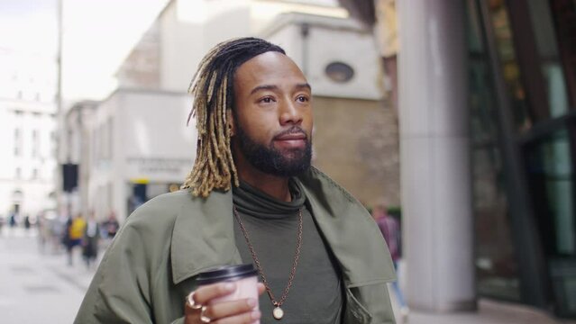 Attractive and confident young black man walking through the city drinking from a coffee cup, in slow motion