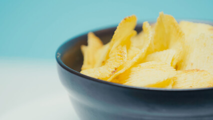 close up view of crunchy and ridged potato chips in bowl on blue with copy space.