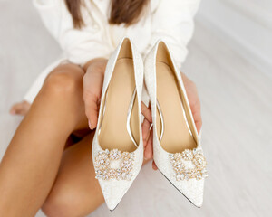 Beige shoes. The girl holds in her hands nude heels for a wedding with gold jewelry