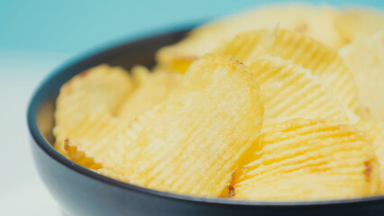 close up view of crunchy and rippled potato chips in bowl on blue.