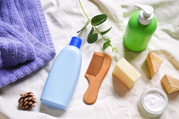 Purple towel, blue shampoo bottle, green liquid soap packaging, face cream and wooden comb flat lay photography. Bath products, toiletries kit