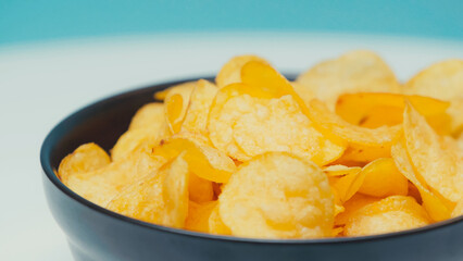 close up view of crispy and ridged potato chips in bowl on blue.