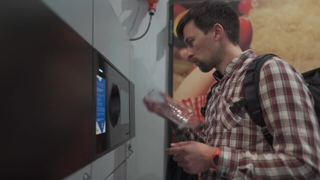 Male returns plastic bottles, reusable containers to reverse vending machine in Munich, Germany supermarket. Man using bottle deposit point. Automatic bottle recycling machine for collection plastic. 