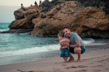 Papá e hijo bebé niño sonriente en la playa jugando y divirtiendose 