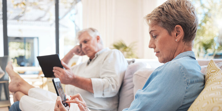 Relax senior couple on sofa with smartphone and tablet technology to watch film while networking on social media with home wifi. Elderly woman and man on couch with digital or online internet content