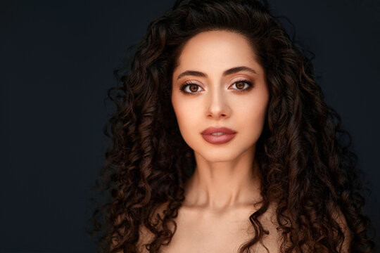 Curly haired woman beauty portrait against dark grey background.