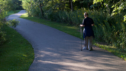 A senior male walking in the public park with walking trekking poles