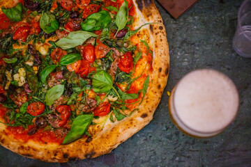 Pizza napoletana con pomodorini, basilico fresco, aglio, origano e olio accompagnata da una birra ghiacciata in una pizzeria napoletana 