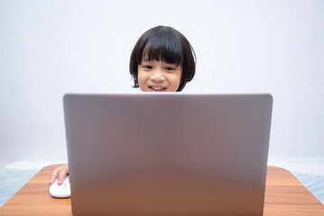 Cute smart Asian boy is happily using his laptop to study online by himself at home. Online learning concept.Self-Study.