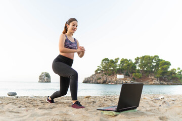 Fototapeta na wymiar Young fit girl doing exercise while watching online tutorial lesson on laptop. Beautiful athletic girl in leggings and top practicing yoga or workout. Sport, healthy lifestyle, virtually