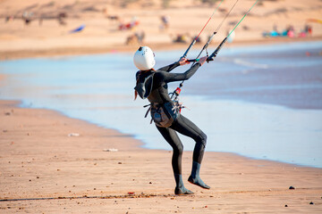 Caucasian woman kitesurfer in a neoprene wetsuit  on a sandy beach on the shore holding her kite in the wind