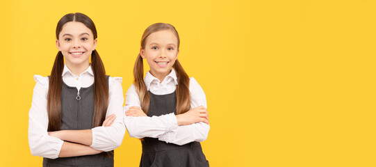 School girls friends. Happy kids wear school uniform keeping arms crossed yellow background, September 1. Horizontal isolated poster of school girl student. Banner header portrait of schoolgirl.