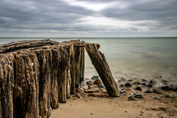 Beach on the Danish Baltic Sea near Sønderborg, Denmark. cloudy sky. In the foreground pier leads into the sea