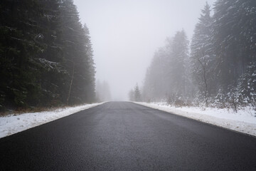 Obraz premium Asphalt road between trees and snow on a foggy day in winter
