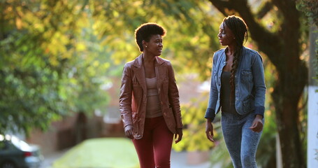 Two women talking outside while walking. African friends in conversation outdoors