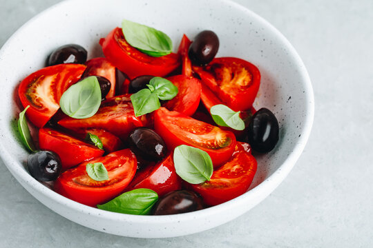Tomato olive salad with fresh basil in white bowl