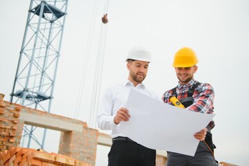 engineer architect with hard hat and safety vest working together in team on major construction site