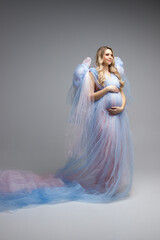Pregnancy woman with blond hair in blue dress. A young pregancy woman in blue dress. Maternity style. Vertical photo. 