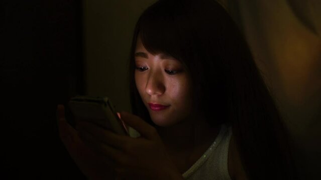 暗闇でスマートフォンを操作する女性