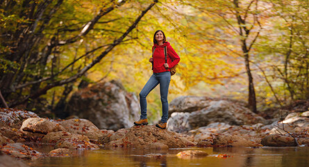 Naklejka na ściany i meble Travel and road trip concept at autumn. Adventure and active lifestyle in nature. Tourist hiking in forest. Asian woman in red hoodie walks in forest. Wanderlust concept.