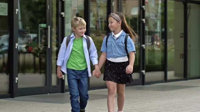 School friendship. A boy and a girl, primary school students, walk out of the school building holding hands.