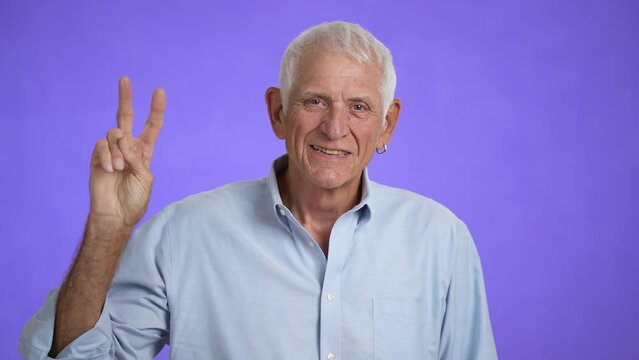 Senior man with flowers in gray-hair showing peace victory sign gesture, hoping for success and win, smiling and optimistic expression. Elderly grandfather