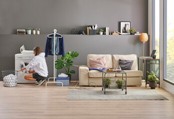Obraz premium Girl is cleaning her clothes, washing machine, laundry style, decorative room, sofa and grey wall background.