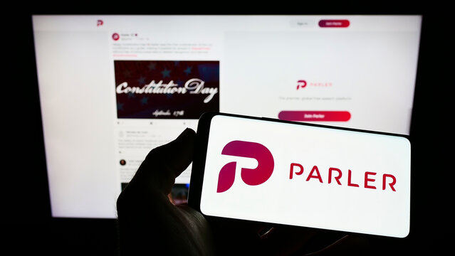 Stuttgart, Germany - 09-18-2022: Person holding mobile phone with logo of American social networking company Parler Inc. on screen in front of web page. Focus on phone display.