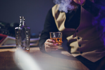 A close-up shot of a man drinking whiskey and smoking a cigarette in a tavern at night.
