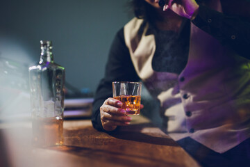 A close-up shot of a man drinking whiskey and smoking a cigarette in a tavern at night.
