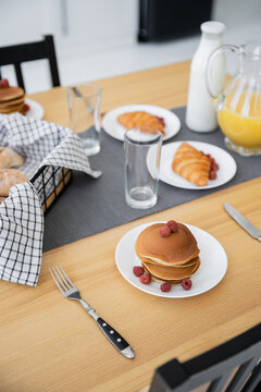 tasty pancakes near baked croissants and jug with orange juice on table.