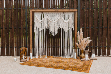 Beautiful bohemian type arch decoration on outdoor wedding ceremony venue on backyard. Florist flower compositions with pampas grass near carpet, string fairy lights.