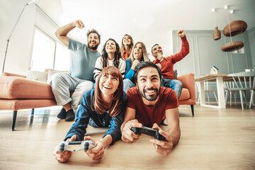 Happy friends playing together video game at home - Group of young people having fun sitting on the...