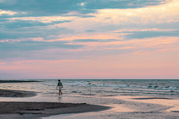 Fototapeta na wymiar A girl walks along an empty beach