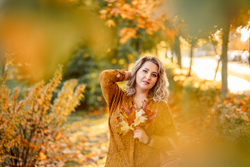Autumn portrait of a plus-size girl with a bouquet of yellow leaves in her hands