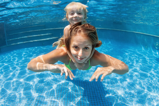 Happy family - young mother, baby boy learn to swim, dive underwater. Jump with fun in swimming pool. Healthy lifestyle, active parents, people water sports activities on summer holidays with kids.