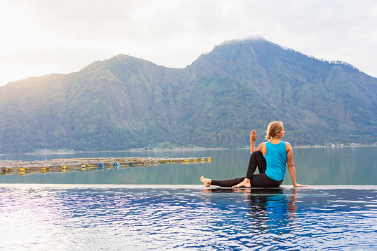 Young girl practice yoga at Batur volcano hot spring spa. Travel in Kintamani, Bali. Woman meditate in infinity pool with lake view. Healthy lifestyle, recreational activity on summer holiday.