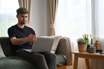 Asian man working with laptop while sitting on the sofa, Domestic life at home concept.