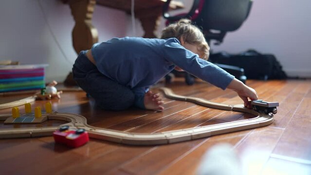 Little boy playing with toys on hardwood floor. Child plays with traditional railroad wooden tracks at home. Male kid holding objects