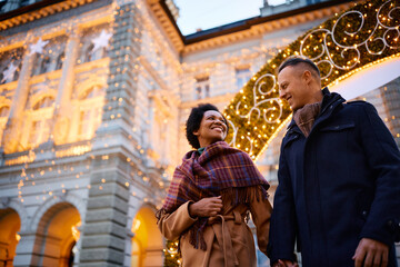 Below view of happy couple holding hands and enjoying in walk in Christmas decorated city.