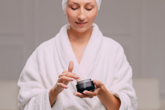 Young attractive woman in a bathrobe applies cream on her face in the bathroom.